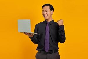 Portrait of excited Asian businessman holding laptop over yellow background photo