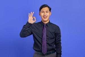 Smiling handsome young businessman showing ok gesture on purple background photo