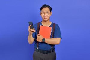 Smiling young Asian man holding cell phone and notebook on purple background photo