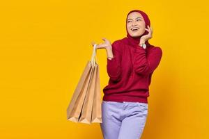 Beautiful Asian woman showing several shopping bags and looking sideways with smiling face on yellow background photo