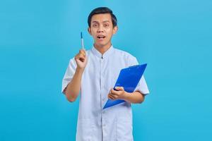 Attractive young Asian male nurse holding pen and having good idea isolated over blue background photo