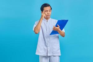 Young male nurse concentrating writing prescription notes on clipboard over blue background photo