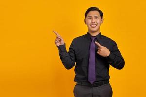 Smiling young Asian man pointing fingers at copy space on yellow background photo