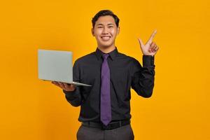Smiling Asian businessman holding credit card pointing finger at copy space on yellow background