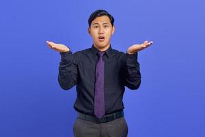 Portrait of shocked young handsome businessman showing copy space on palm on purple background photo
