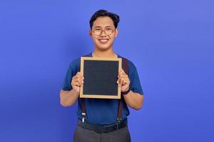 Smiling handsome young man showing blank board on purple background photo