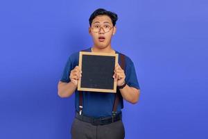 Shocked handsome young man showing blank board on purple background