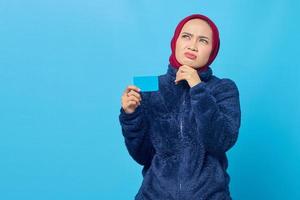 retrato, de, pensativo, joven, mujer asiática, tenencia, tarjeta de crédito, y, mirar hacia arriba, en, fondo azul