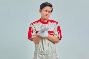 Portrait of handsome man wearing mechanical uniform suffering from pain in hands and fingers on gray background photo