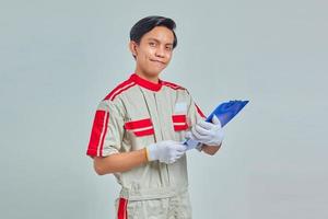 Happy young asian mechanic holding clipboard isolated over gray background photo