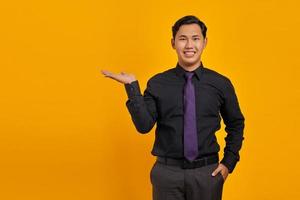 Smiling young handsome businessman showing copy space on palm on yellow background photo