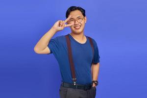 Portrait of cheerful asian man showing peace sign over eyes over purple background photo