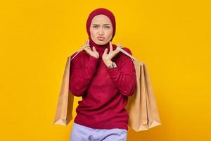 Portrait of beautiful excited Asian woman holding shopping bags on yellow background photo