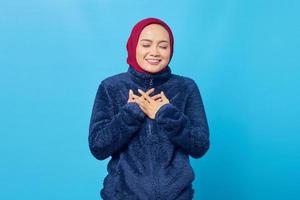 Smiling young Asian woman keeping both palms on a chest isolated over blue background photo