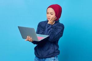 Beautiful Asian woman using laptop with confused expression looking at and holding cheek with palm photo