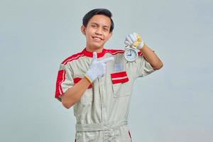 Portrait of smiling handsome man wearing mechanical uniform holding alarm clock on gray background photo