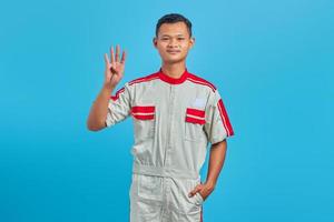 Portrait of smiling young Asian mechanic making number four sign with finger isolated on blue background