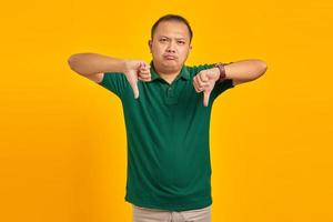 Hombre asiático joven enojado que muestra el rechazo con el pulgar hacia abajo gesto sobre fondo amarillo foto