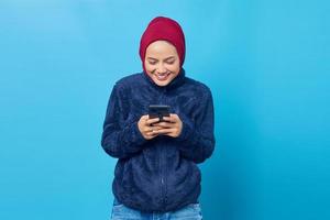 Portrait of beautiful smiling Asian woman receiving text message from boyfriend on blue background photo