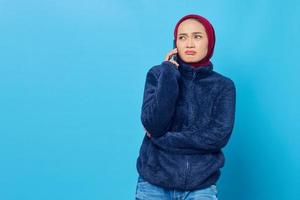 Confused young Asian woman talking on a mobile phone with her boyfriend isolated on blue background photo