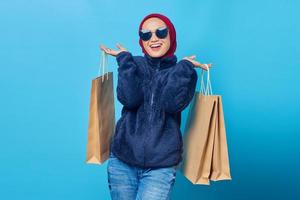 Retrato de alegre hermosa mujer asiática sosteniendo bolsas de compras sobre fondo azul.