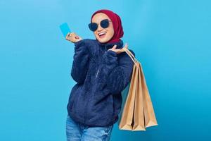 Smiling young Asian woman holding shopping bags and credit card on blue background photo