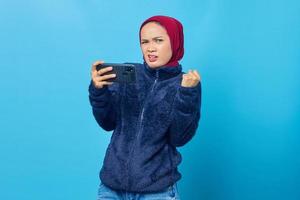 Sad young beautiful woman playing a game on mobile phone on blue background photo