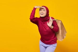 Cheerful young Asian woman excited and holding shopping bags on yellow background photo