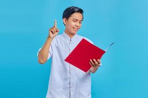 Retrato de alegre enfermero sosteniendo la carpeta de pie y apuntando hacia arriba sobre fondo azul. foto