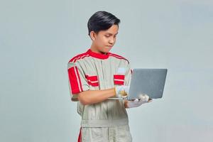 Portrait of smiling handsome mechanic man wearing uniform holding and using laptop on gray background photo