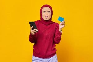 Portrait of shocked young Asian woman holding smartphone while showing credit card