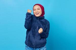 Cheerful young Asian woman celebrating victory dan euphoric over achievement on blue background photo