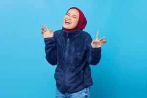 Attractive young Asian woman with laugh face and raised hand isolated over Blue background