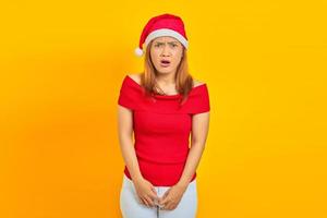 Portrait of surprised young Asian woman with open mouth and wearing Christmas hat on yellow background photo
