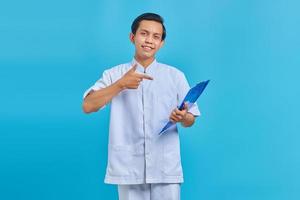 Portrait of asian male nurse pointing finger at clipboard and smiling on blue background photo