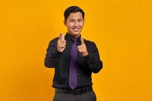 Handsome young businessman smiling while pointing at camera on yellow background photo
