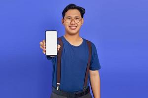 Asian young man showing blank smartphone screen with hand to camera on purple background photo