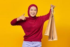 Beautiful Asian woman showing some shopping bags and giving thumbs up with smiling face on yellow background photo