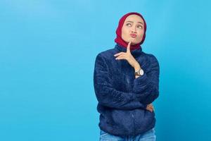 Pensive young Asian woman thinking about something on blue background photo