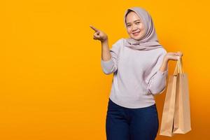 Portrait of excited asian woman holding shopping bag and pointing finger at empty space photo