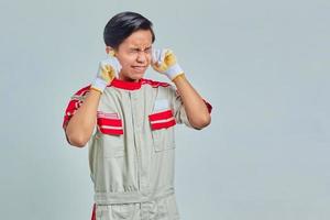 Retrato de frustrado joven apuesto mecánico cubriendo las orejas con los dedos sobre fondo gris