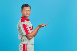 Portrait of smiling young Asian mechanic showing copy space in palm over blue background photo