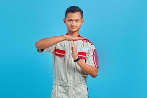Portrait of young Asian mechanic showing timeout gesture over blue background photo