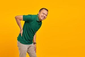 Retrato de un hombre asiático guapo que sufre de dolor de espalda y toca la espalda con las manos sobre fondo amarillo