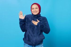 Portrait of smiling young Asian woman swearing with hands on chest and open palms on blue background photo