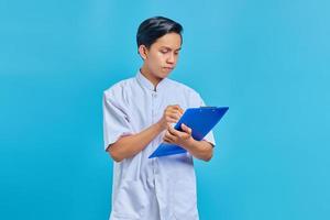 Smiling young male nurse taking notes on clipboard on blue background photo