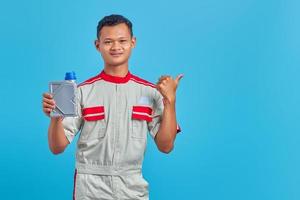 Portrait of smiling young Asian mechanic showing engine oil plastic bottle and pointing to empty space over blue background photo