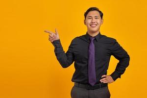 Portrait of smiling young asian businessman pointing finger at copy space on yellow background photo