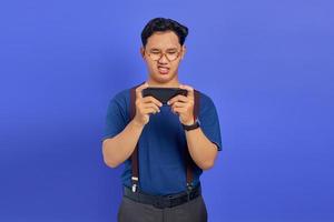 Sad handsome young man playing game on mobile on purple background photo