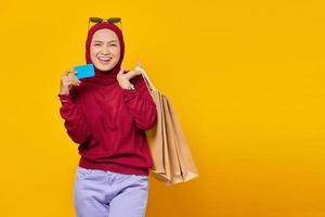 Smiling young Asian woman holding credit card and shopping bags on yellow background photo